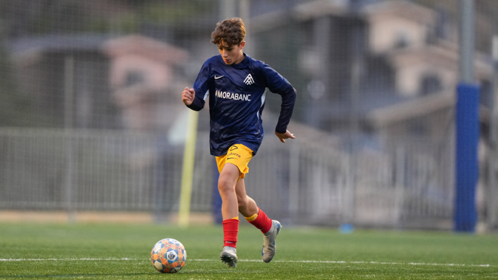 Un jugador de fútbol infantil corriendo con el balón en un campo