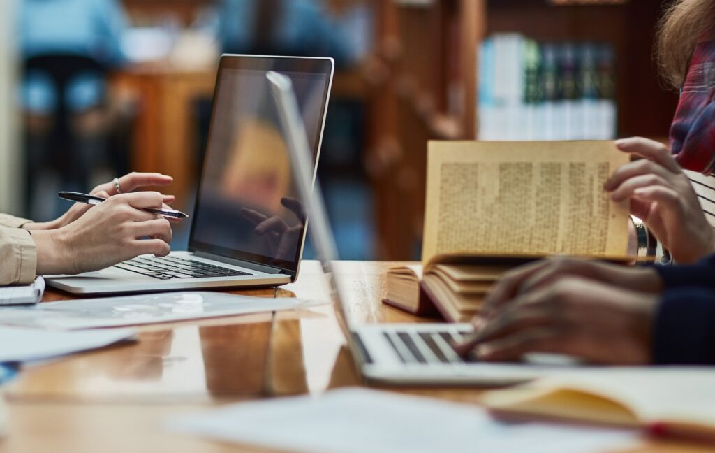 Manos de estudiantes trabajando en laptops y libros en una mesa