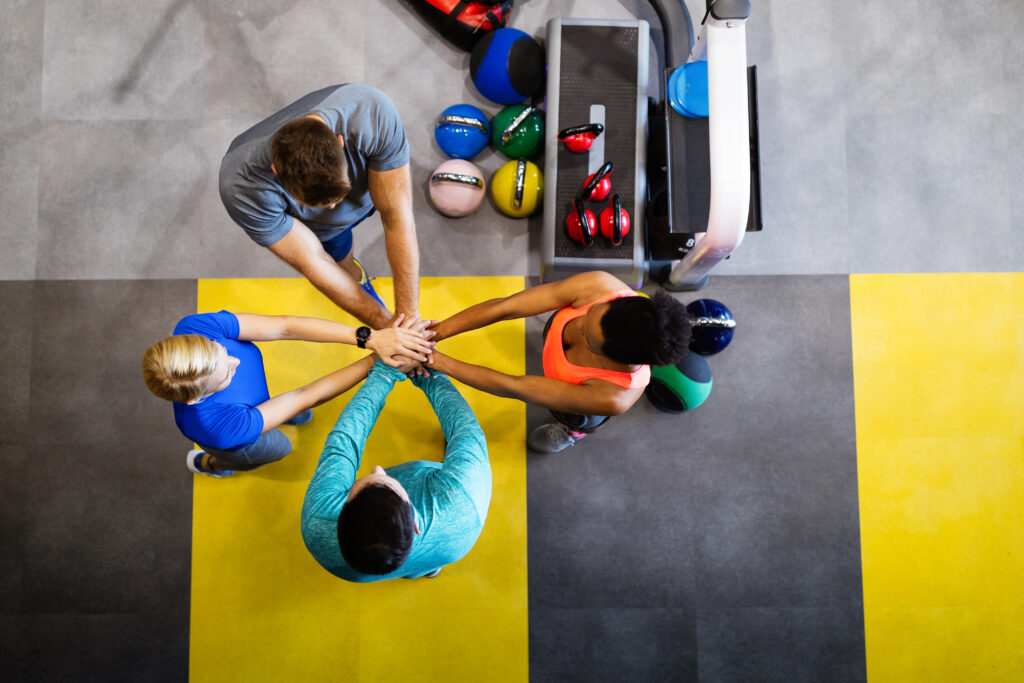 Grupo de personas en un gimnasio uniendo manos en apoyo mutuo.