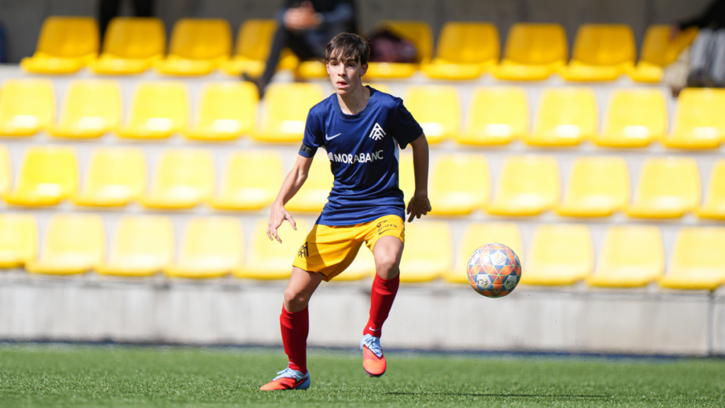 Jugador del Cadete del Andorra corriendo con un balón en el campo