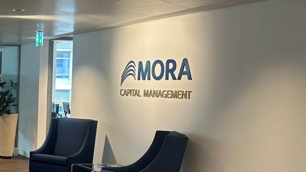 Oficina de Mora Capital Management con logo en la pared