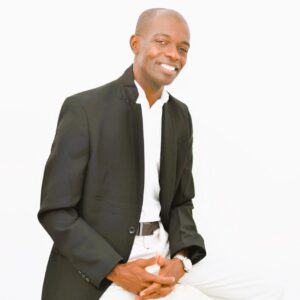 Hombre sonriente vestido de traje negro y camisa blanca en fondo blanco