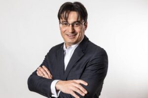 Retrato de un hombre con gafas y traje sonriendo con los brazos cruzados