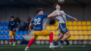 Jugadores del Juvenil compiten por el balón en un partido de fútbol