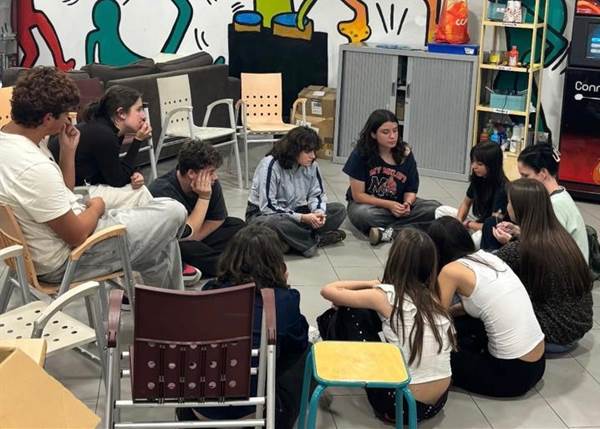 Grupo de jóvenes en ensayo teatral, sentados en círculo en un espacio comunitario.