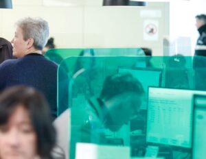 Personas en un entorno de oficina con pantallas de computadora y paneles de separación