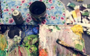 Paleta de pintura con colores mezclados y pincel sobre mesa decorada