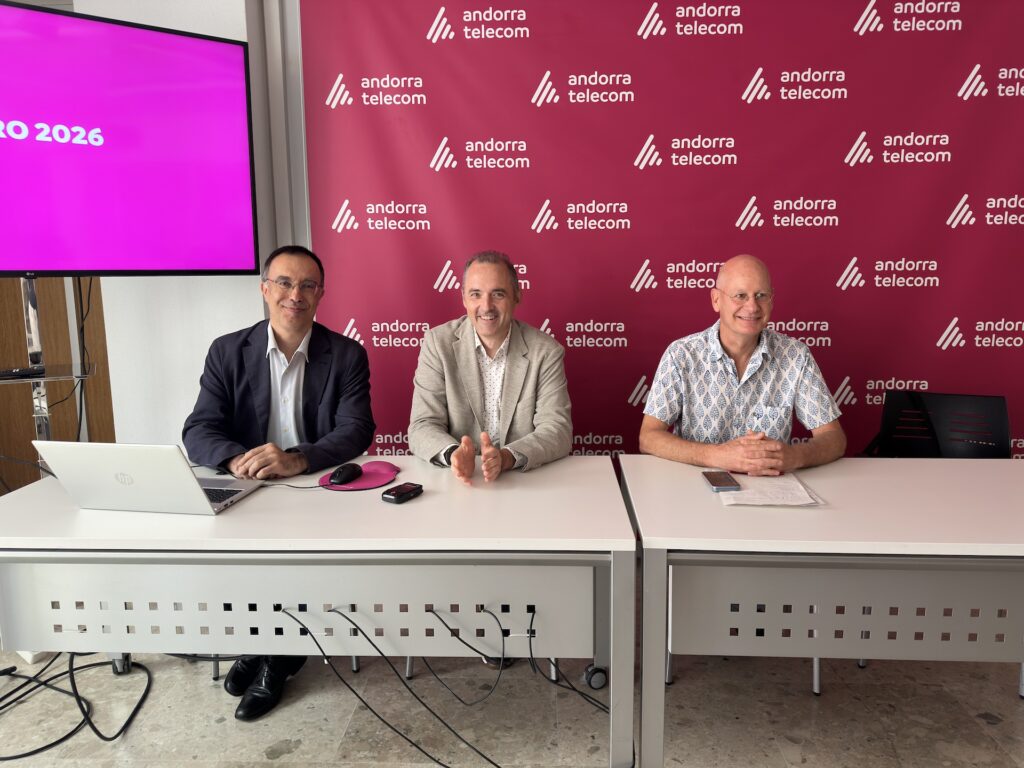 Tres personas sentadas en una mesa con el logo de Andorra Telecom de fondo
