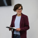 Persona sonriente sosteniendo documentos en un evento sobre archivos y patrimonio.