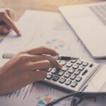 Persona usando calculadora sobre documentos de auditoría y gráficos