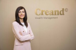 Mujer sonriente con brazos cruzados frente a un logo de Creand Wealth Management