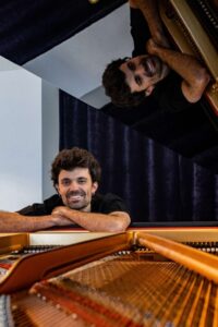 Kic Barroc sonríe mientras se apoya en un piano de cola.