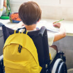 Niño en silla de ruedas estudiando con mochila amarilla