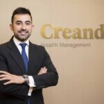 Hombre sonriente en traje frente a un logo de Creand Wealth Management