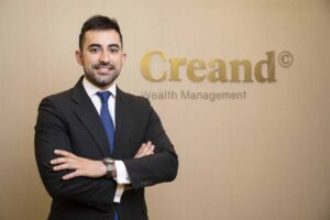 Hombre sonriente en traje frente a un logo de Creand Wealth Management