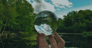 Persona sosteniendo una esfera de cristal reflejando un paisaje natural