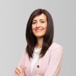 Mujer sonriente con cabello largo y oscuro, vestida con chaqueta rosa