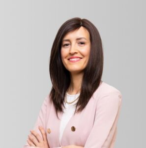 Mujer sonriente con cabello largo y oscuro, vestida con chaqueta rosa