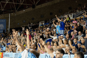 Aficionados aplauden y levantan los brazos en las gradas de un pabellón
