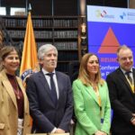 Cuatro personas posan ante banderas y un panel de una reunión iberoamericana.