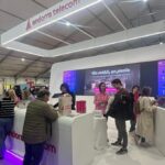 Personas visitan un estand de Andorra Telecom con pantallas y módulos interactivos.