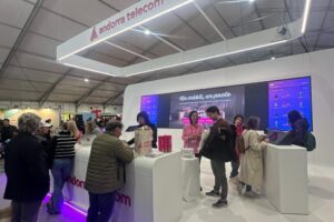 Personas visitan un estand de Andorra Telecom con pantallas y módulos interactivos.