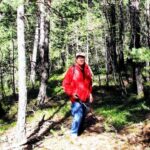 Un hombre con chaqueta roja camina entre árboles por un sendero boscoso.