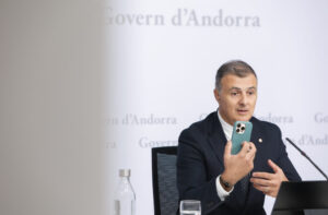 Hombre sentado sostiene un teléfono móvil frente a un fondo del Gobierno de Andorra