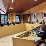 Personas sentadas alrededor de una mesa; algunas levantan la mano durante una sesión.