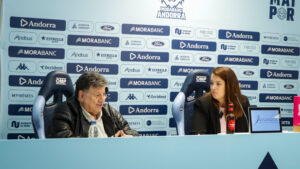 Dos personas sentadas ante una mesa durante una rueda de prensa con logotipos detrás.
