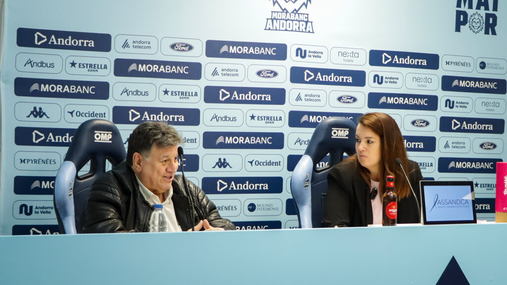 Dos personas sentadas ante una mesa durante una rueda de prensa con logotipos detrás.